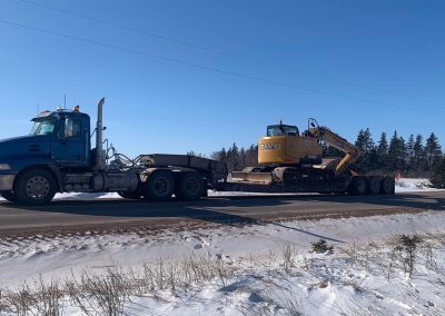 Landmark Construction PEI transport hauling excavator on snowy road.